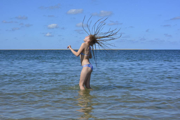 Девушка стоит в море и бросает свои длинные влажные волосы назад, вода брызгает в воздух
 - Фото, изображение