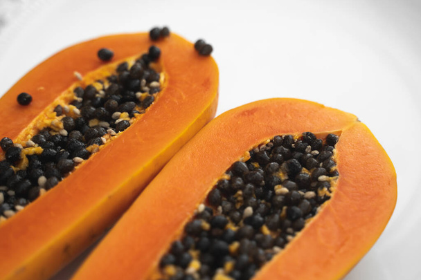 Half cut ripe papaya with seed on a white plate. Slices of sweet papaya with a white background. Halved papayas. Healthy exotic fruits. Vegetarian food. - Фото, зображення