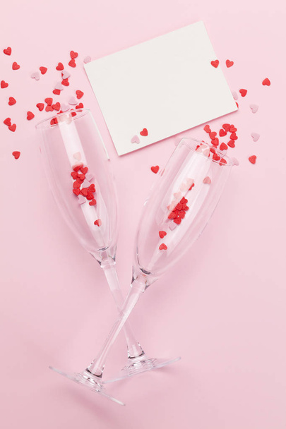 Champagne glasses and heart shaped sweets holiday template. Christmas, Birthday or Valentines'day over pink background. Top view with space for your greetings. Flat lay - Фото, зображення