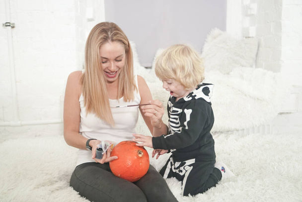 Giovane donna e il suo bambino hanno divertimento autunno con zucca sul davanzale bianco, ragazzo vestito in costume scheletro
 - Foto, immagini