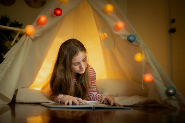 feliz niña leyendo libro y jugar a acampar en tiendas de campaña en casa
 - Foto, imagen