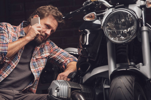 Homme parlant au téléphone agenouillé à moto
 - Photo, image