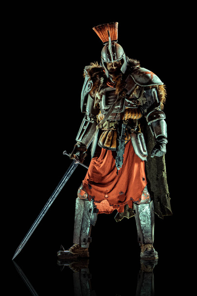 Krachtige ridder in het harnas met het zwaard. Geïsoleerd op zwarte achtergrond. - Foto, afbeelding