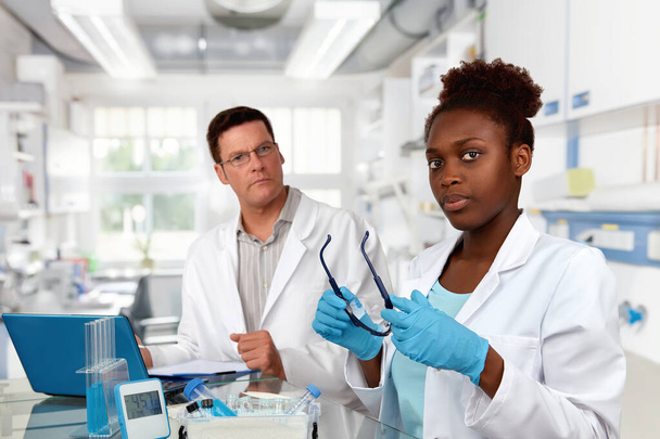 Scientists, Caucasian male and African female, work in laborator - 写真・画像
