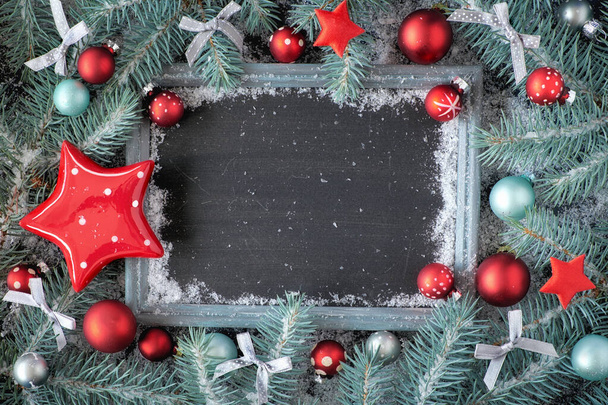Groene en rode kerstachtergrond met versierd krijtbord. Versierde dennentwijgen rond krijtbord op rustiek hout met sneeuw. Bovenaanzicht met kopieerruimte. - Foto, afbeelding