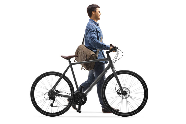 Cara em roupas jeans andando e empurrando uma bicicleta
 - Foto, Imagem