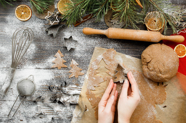 Ženské ruce vyřezávají vánoční sušenky figurky ve tvaru vánočního stromku na kuchyňském dřevěném stole, horní pohled. Vánoční náladu pozadí. plochý ležel. - Fotografie, Obrázek