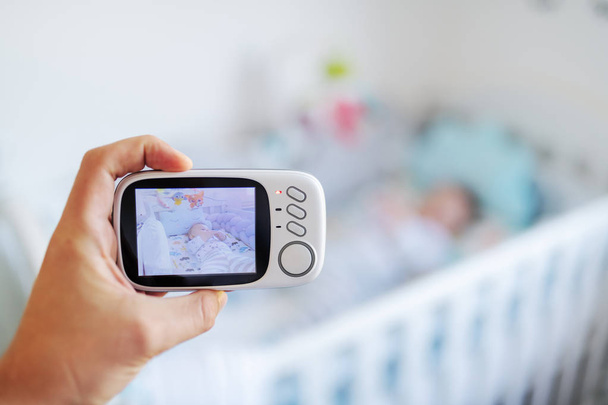 Крупним планом рука тримає дитину тепер сучасний дитячий монітор і записує дитину в ліжечко
. - Фото, зображення
