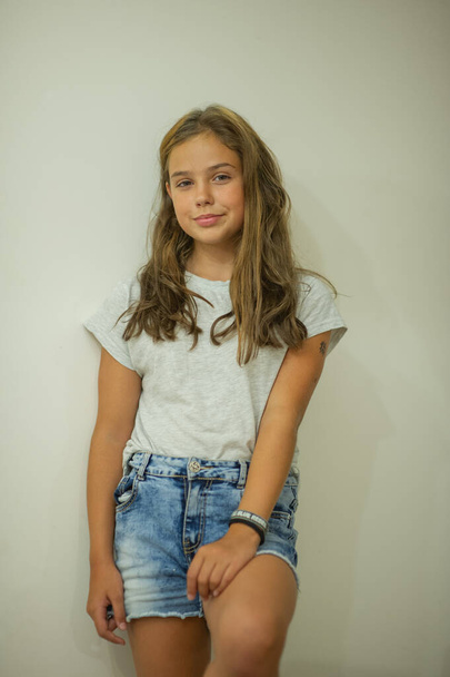 Porträt eines stilvollen jungen schönen Mädchens, das in einem grauen T-Shirt auf weißem Hintergrund lächelt, natürliches Aussehen, lange braune Haare, Jeans, lässiger Stil - Foto, Bild