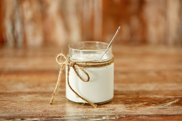 yogurt or sour cream in glass jar on wooden table - Fotoğraf, Görsel