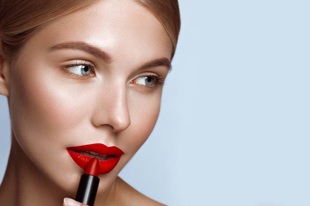 Beautiful girl with red lips and classic makeup with lipstick in hand. Beauty face - Foto, afbeelding