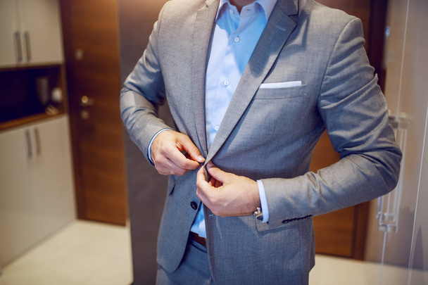 Κόψτε την εικόνα του αριστοκρατικού επιχειρηματία δένοντας το σακάκι του, ενώ στέκεται στο διάδρομο στο σπίτι. - Φωτογραφία, εικόνα
