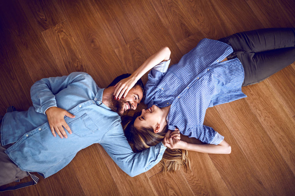 Top view of attractive caucasian couple in love lying down on floor, cuddling and looking at each other. - 写真・画像