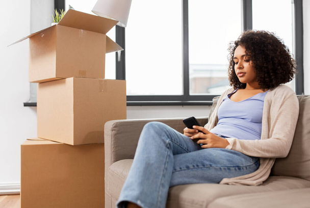 woman with smartphone and boxes moving to new home - Foto, Bild
