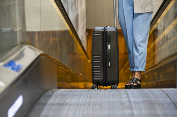 Girl is groing up on escalator with suitcase during holiday trip at airport. Traveling, transfer, waiting at airport - Photo, image