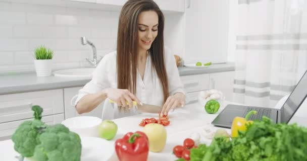 Woman Chopping Vegetables and Looking at Laptop - Video, Çekim