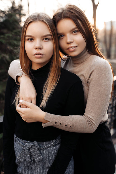 Beautiful two young twin sisters with serious in casual outfit at the autumn park. Looking camera. - Fotó, kép