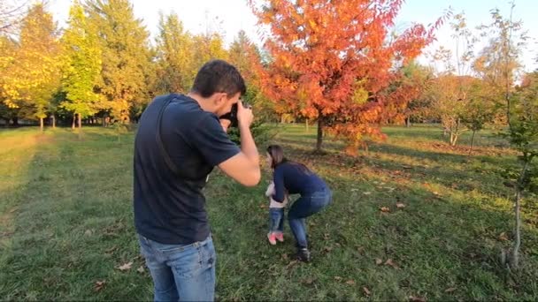 Fotograf robi zdjęcie uroczej dziewczynki bawiącej się z mamą w jesiennym parku. Mała dziewczynka na rękach matek - Materiał filmowy, wideo