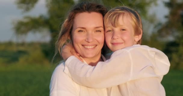 Happy mother  holds her son on hands walking on the meadow in summer.  Mother with 7 year old son strolls on field.   Adult mother with blond boy sauntering in nature. Slow motion. Happiness.      - Materiał filmowy, wideo