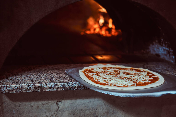Kokki laittaa pizza uuniin leivontaan
 - Valokuva, kuva