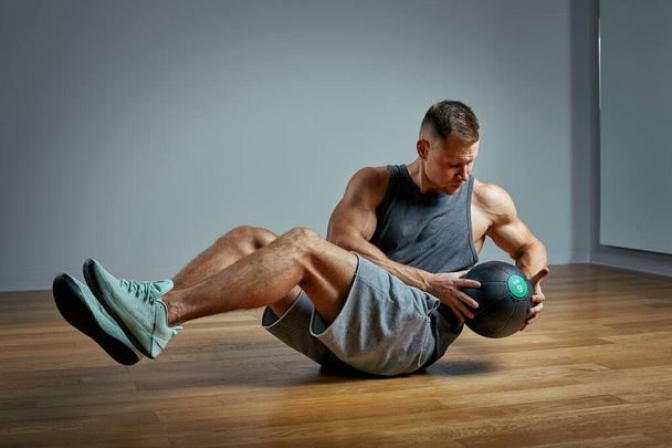 Strong man doing exercise with med ball. Photo of man perfect physique on grey background. Strength and motivation. - Photo, Image