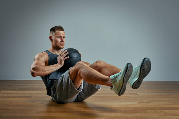 Hombre fuerte haciendo ejercicio con pelota médica. Foto de hombre físico perfecto sobre fondo gris. Fuerza y motivación
. - Foto, imagen