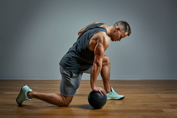 Strong man doing exercise with med ball. Photo of man perfect physique on grey background. Strength and motivation. - Photo, image