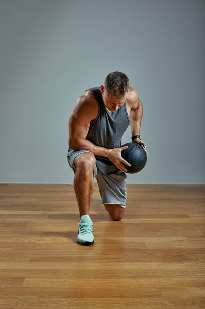 Homem forte a fazer exercício com a bola de medicina. Foto do homem físico perfeito sobre fundo cinza. Força e motivação
. - Foto, Imagem
