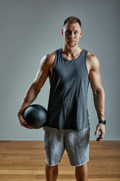 Strong man doing exercise with med ball. Photo of man perfect physique on grey background. Strength and motivation. - Foto, afbeelding