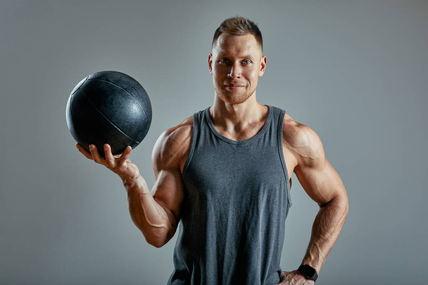 Vahva mies treenaa lääkintäpallon kanssa. Kuva ihmisen täydellinen ruumiinrakenne harmaalla pohjalla. Vahvuus ja motivaatio
. - Valokuva, kuva