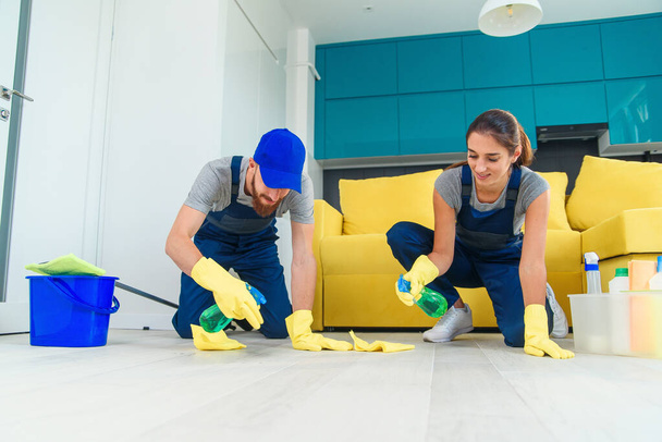 Smiling girl and handsome bearded man in workwears washing the parquet with the cleaning items and wipping with rags - Photo, Image