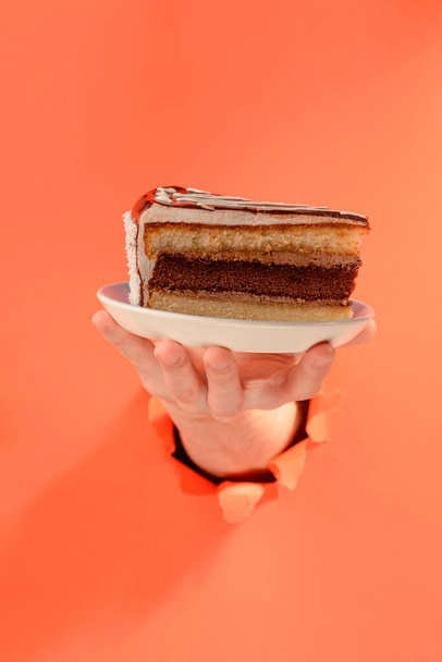 Hand serving a chocolate cake through a torn hole in red paper background. - Fotografie, Obrázek