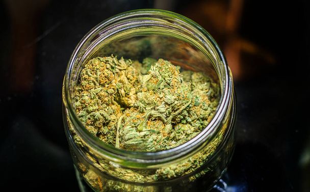 Cannabis flower buds in glass jar against dark background - Photo, Image