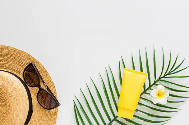 Top view of suncream, straw hat, palm leaf, sunglasses. spf cream on white background with copy space. Directly above. Bright summer, vacations, skincare concept. Flat lay, template, mockup - Fotó, kép