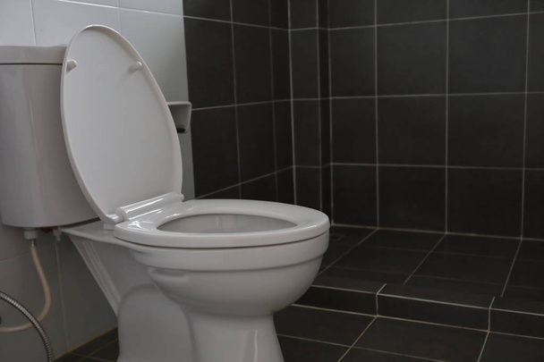nowoczesny design małej łazienki z białą toaletą szafę na wodę i używane czarne płytki ściany i podłogi - Zdjęcie, obraz
