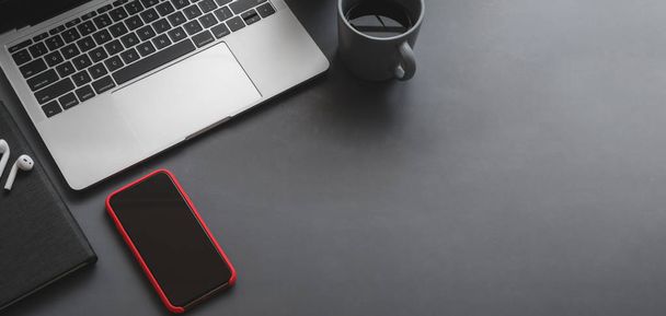 Ansicht des modernen Büroraums mit Laptop und Smartphone auf schwarzem Tisch mit Kopierraum  - Foto, Bild