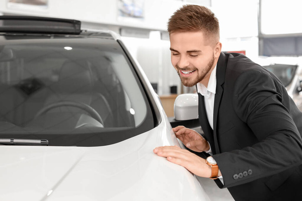 Щасливий чоловік-покупець біля нової машини в салоні
 - Фото, зображення