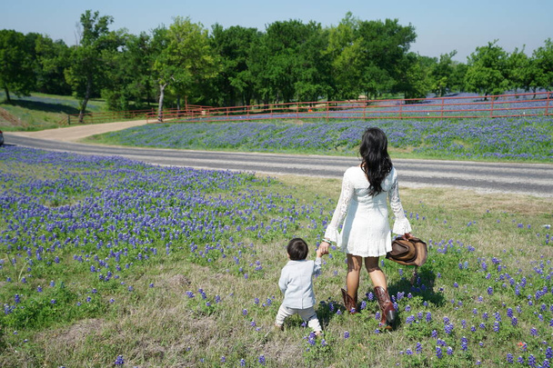 Žena a chlapec kráčí a dívá se na divoké květy Bluebonnet v plném květu během jara kolem Texas Hill Country, USA  - Fotografie, Obrázek