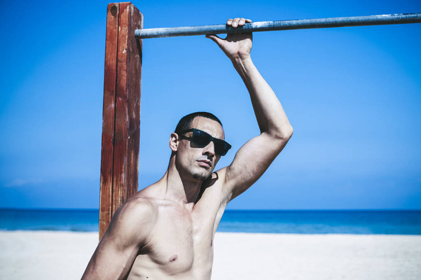 young muscular man resting and posing on the beach. Wearing sunglasses - Photo, image