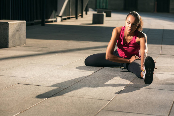 Calm young sporty lady sitting on the ground and pulling her legs while warming up. Template banner - Foto, Imagen