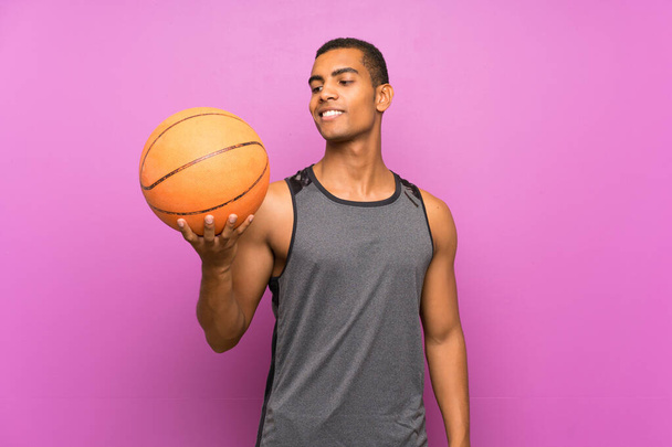 Joven deportista con pelota de baloncesto sobre pared púrpura aislada con expresión feliz
 - Foto, Imagen
