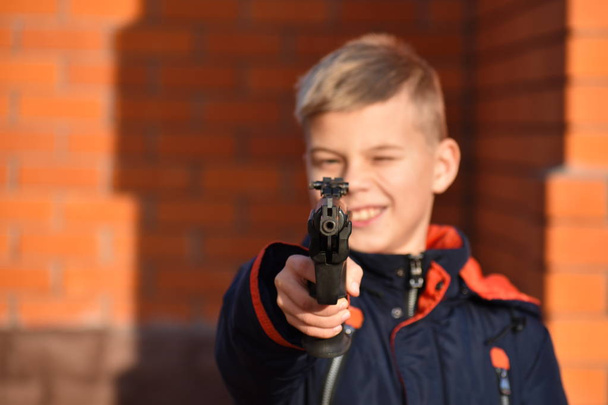 Child with dangerous weapons. Boy shoots  gun. Teenager with a gun. Child learn to shoot. - Foto, Bild