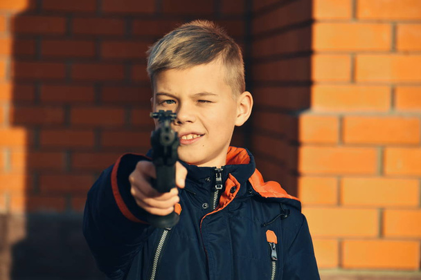 Child with dangerous weapons. Boy shoots  gun. Teenager with a gun. Child learn to shoot. - Фото, изображение