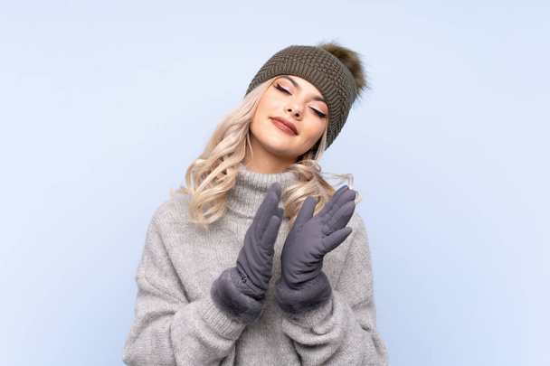 Young teenager girl with winter hat over isolated blue background applauding - Foto, Imagem