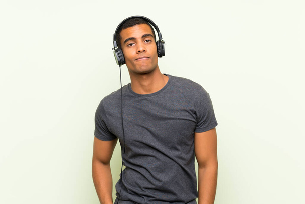 Joven hombre guapo escuchando música con un móvil sobre una pared verde aislada
 - Foto, Imagen