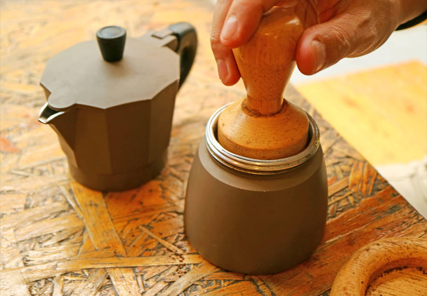 Mano ligeramente golpeando café molido con manipulador de madera para una superficie plana antes de preparar café aromático
 - Foto, Imagen