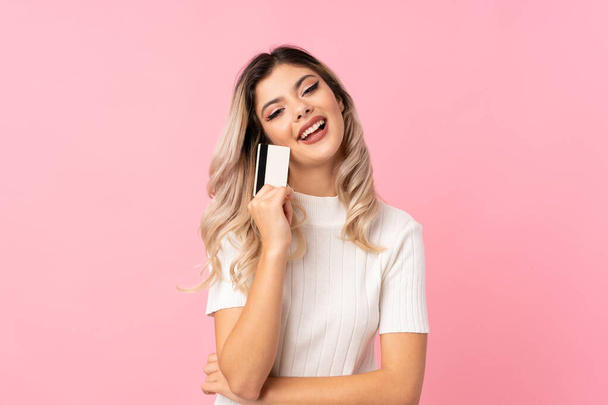 Teenager dívka přes izolované růžové pozadí drží kreditní kartu - Fotografie, Obrázek