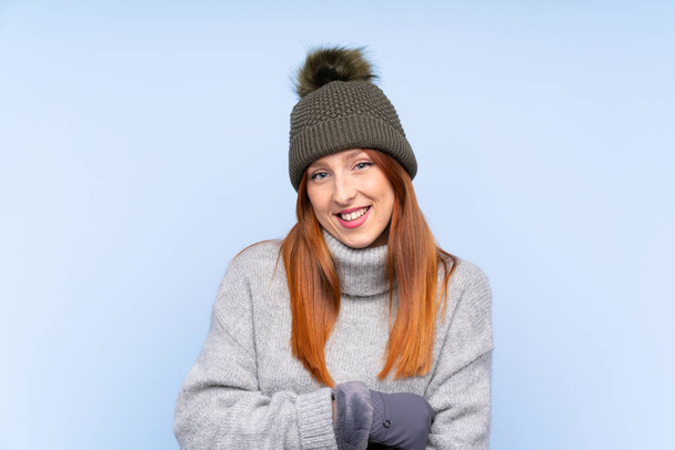 junge rothaarige russische Frau mit Wintermütze über isoliertem blauem Hintergrund lacht - Foto, Bild