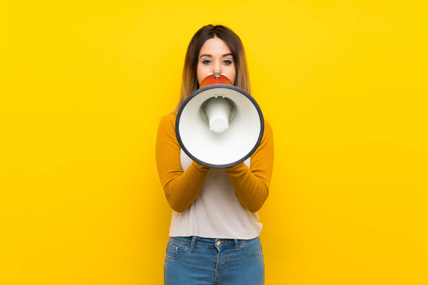 Pretty young woman over isolated yellow wall shouting through a megaphone - Foto, Imagen
