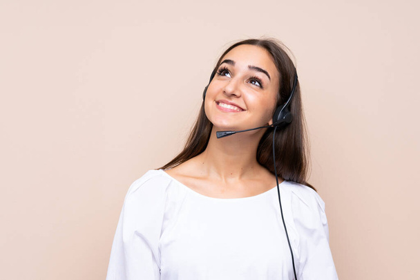Young telemarketer woman over isolated background looking up while smiling - Photo, Image